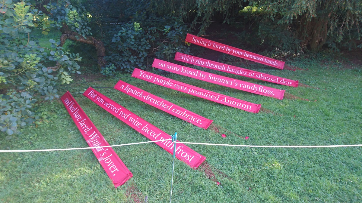 Photo showing the installation of the poem 'Smokebush - A Seasoned Lover'. The banners are in front of the smokebush and reach around in a fan shape.